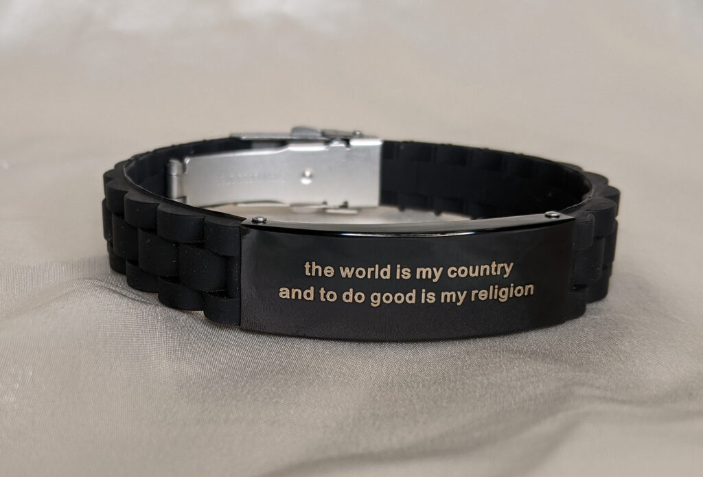 black textured silicone bracelet with silver metal clasp. punk vibe. black metal on bracelet is engraved with the words "the world is my country and to do good is my religion" This is a quote from Thomas Paine.